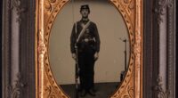 Tintype portrait of a standing Union soldier holding a rifle; a metal posing stand is visible behind him on the right.