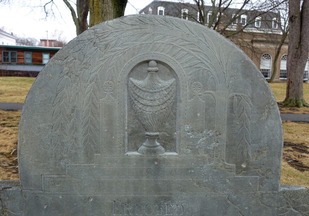 Gravestone carved with an urn beneath a weeping willow, Memorial Cemetery, Westborough, Massachusetts.
